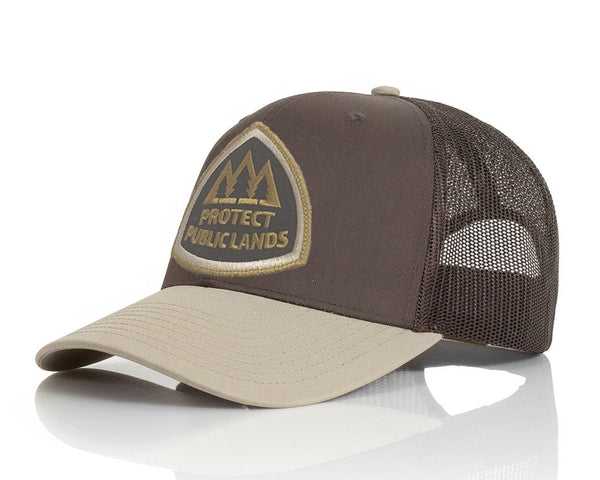 A brown and beige trucker hat with a mesh back and a shield-shaped embroidered patch on the front that reads 'PROTECT PUBLIC LANDS'.