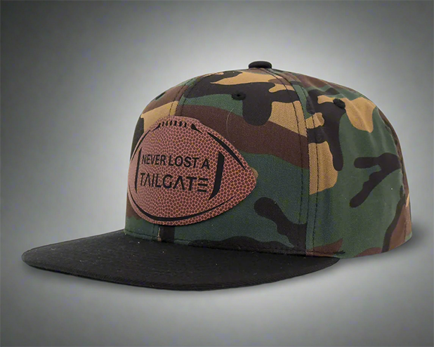 Camo snapback hat with black brim and football patch reading 'Never Lost a Tailgate'.