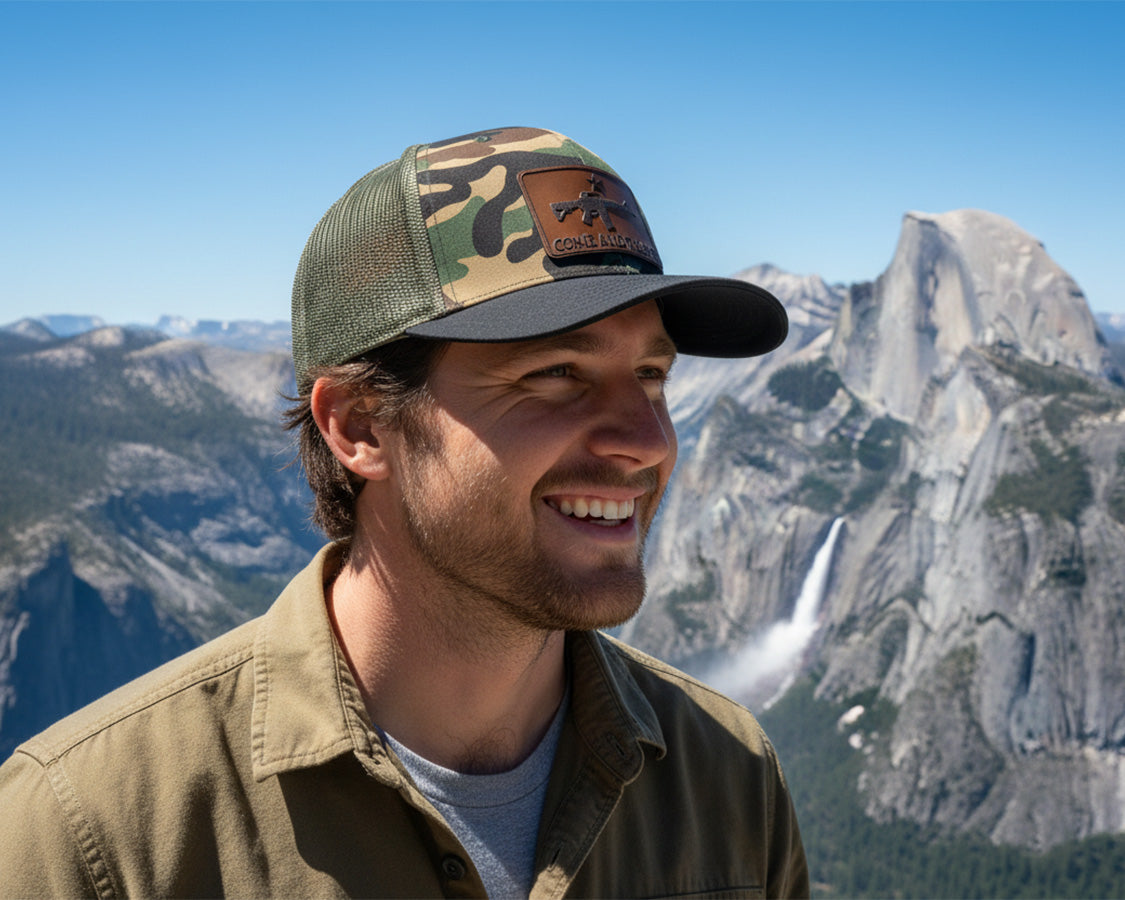Man wearing a camouflage cap and brown jacket with mountains in the background