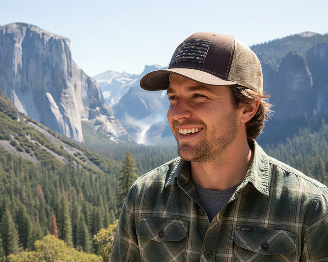 Man wearing a cap and plaid shirt with mountains in the background