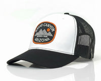 A black and white trucker hat with a curved brim, featuring a circular 'Grand Canyon National Park Arizona' patch on the front. The front panel is white, the brim is black, and the back mesh is black.