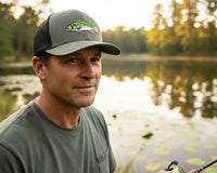 Man wearing a cap with a fish design by a lake