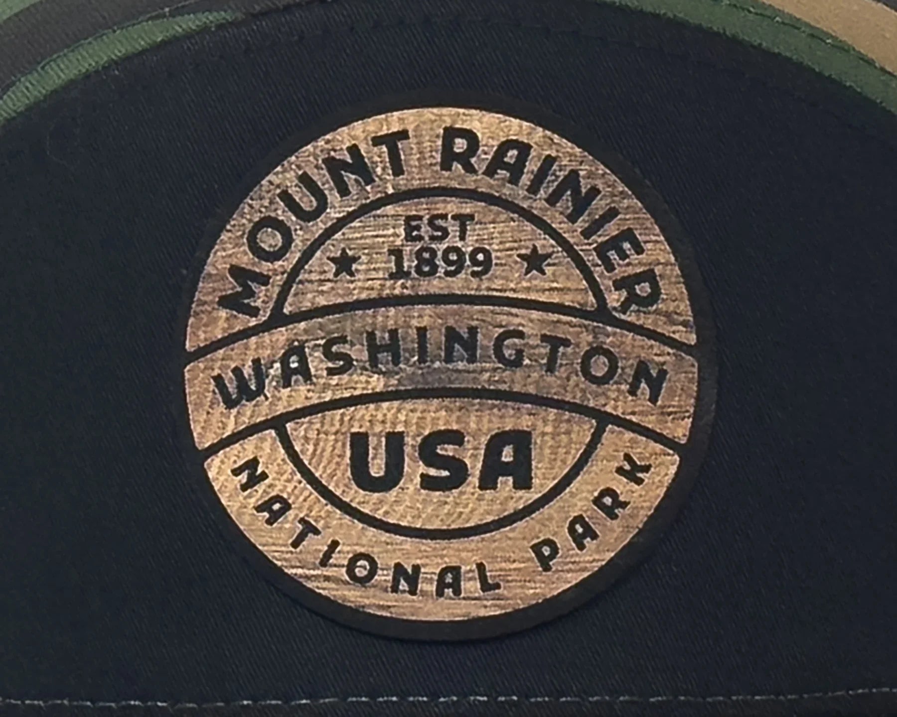 Round wooden emblem with 'Mount Rainier National Park' text on a dark background