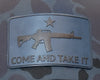 Metallic patch with gun design and 'COME AND TAKE IT' text on a camouflage background