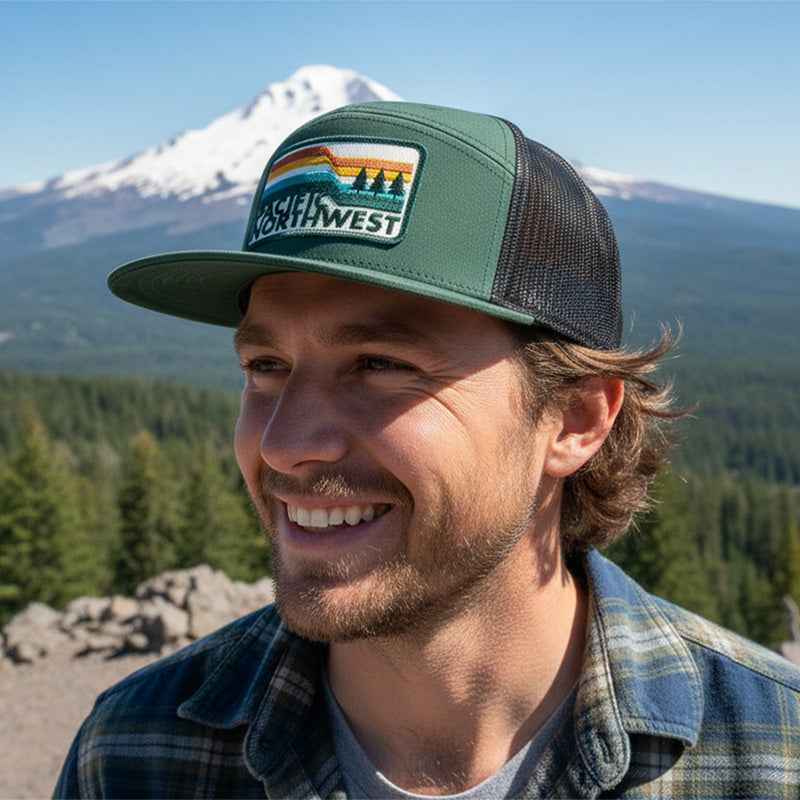 Man wearing a green and black cap with a logo, standing in front of a mountainous landscape.