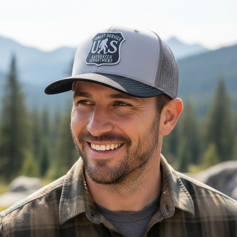 Man wearing a cap with a U.S. Forest Service logo in a mountainous area