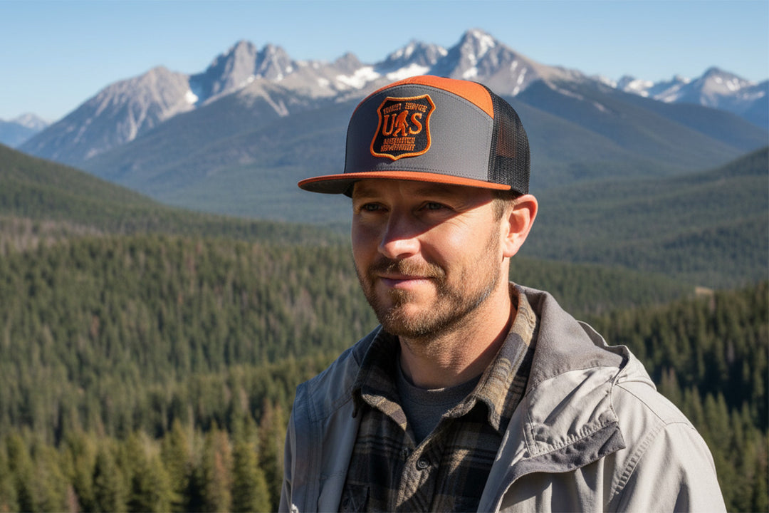 Man wearing a cap with a logo in front of a mountainous landscape