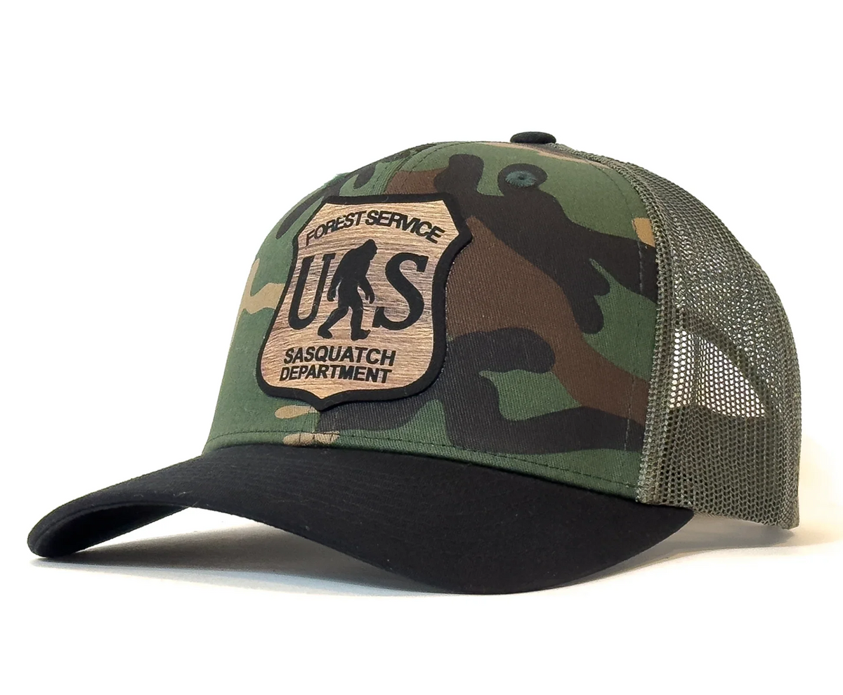 Camouflage cap with a patch labeled 'Forest Service Sasquatch Department' on a white background