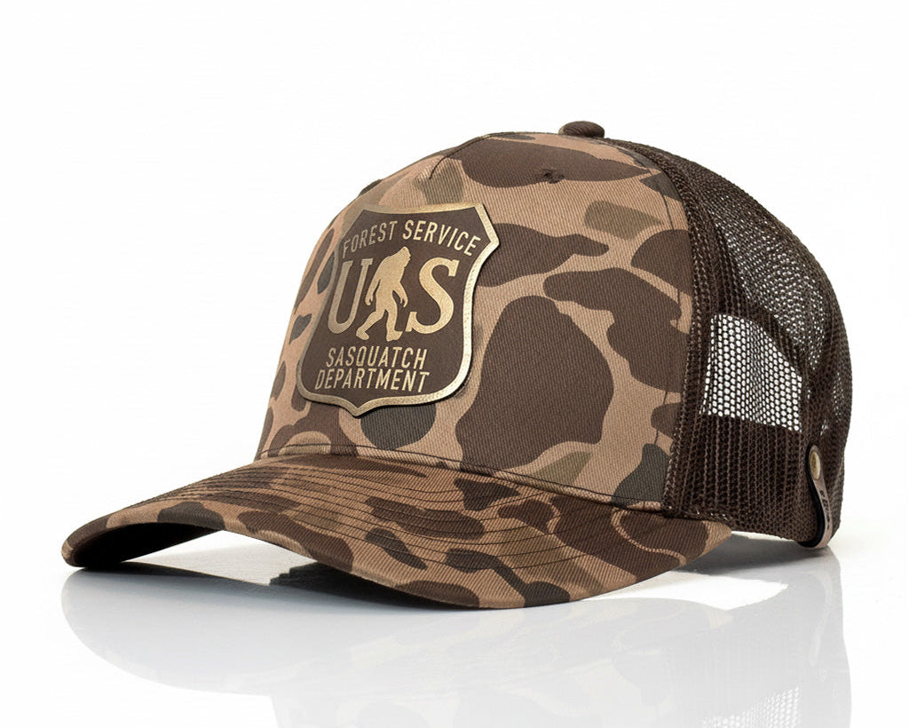 Camouflage cap with 'Forest Service Sasquatch Department' logo on a white background