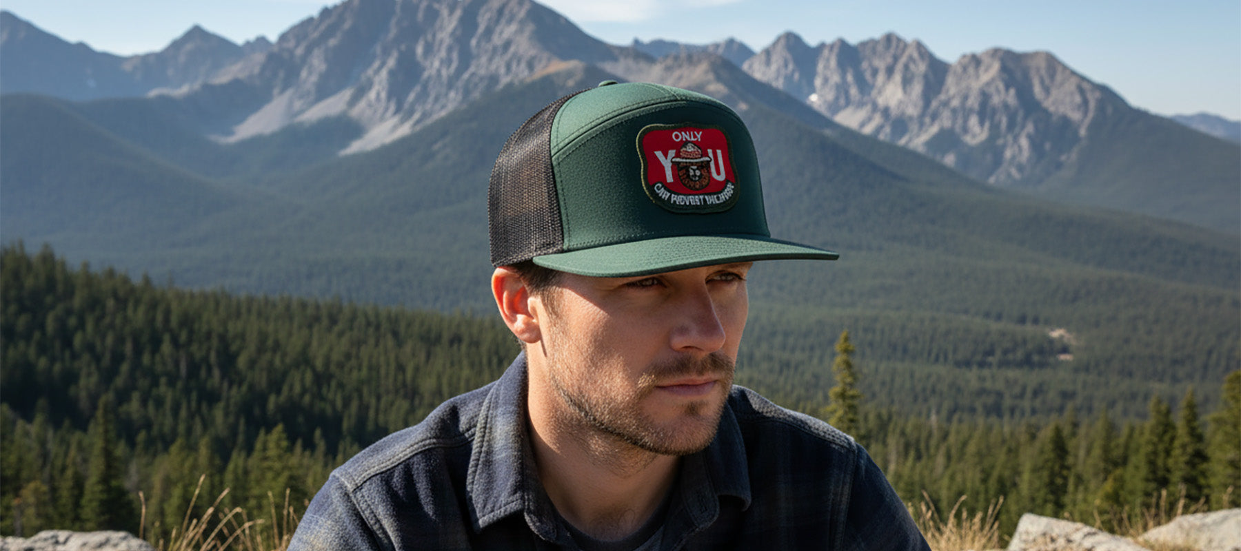 Man wearing a cap with a logo in front of a mountainous landscape