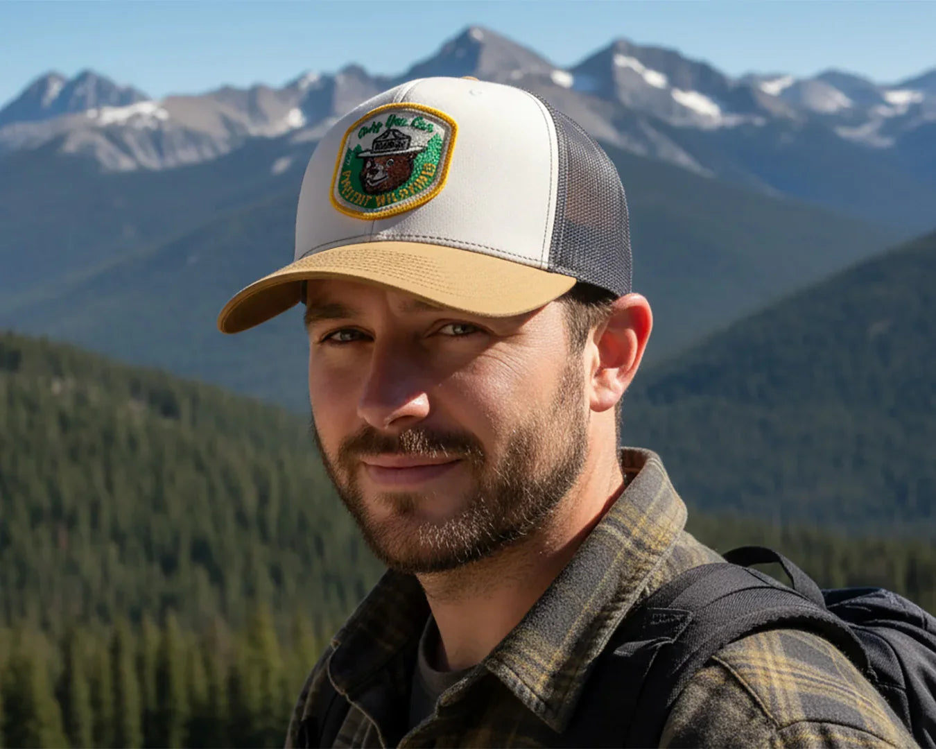 Man wearing a cap with a logo, standing in front of mountains and trees