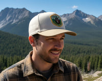 Man wearing a cap with a logo in front of mountainous landscape