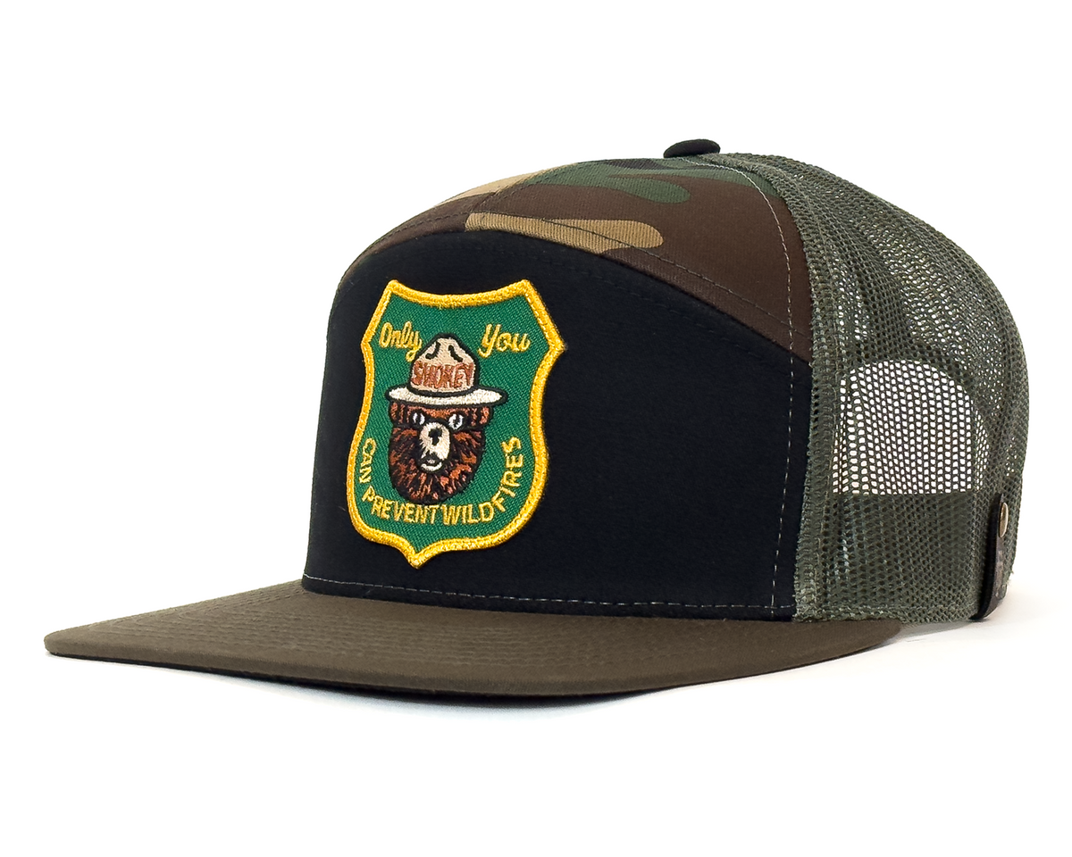 Camouflage and black trucker hat with a bear emblem on a white background