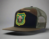 Camouflage and black trucker hat with a bear emblem on a white background