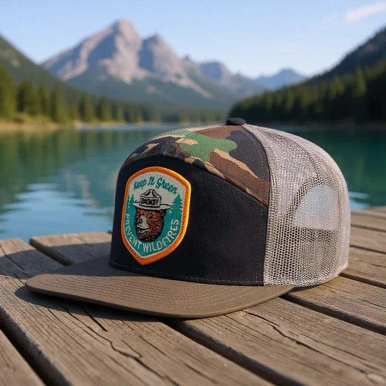 Camo mesh trucker hat with Smokey Bear patch on dock by clear lake and mountain view