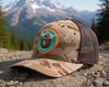 Camouflage cap with a patch on a rocky surface with mountains in the background