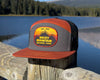 Trucker hat with Rocky Mountain National Park patch on a wooden post by a lake with mountains in the background