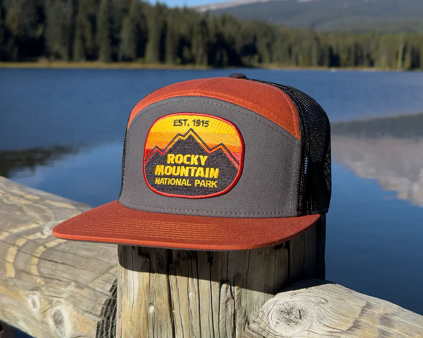 Trucker hat with Rocky Mountain National Park patch on a wooden post by a lake with mountains in the background
