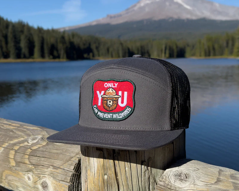 Black cap with a red and green patch on a wooden post by a lake with mountains in the background