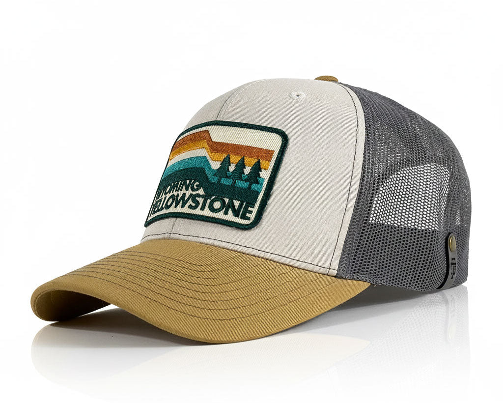 A trucker-style baseball cap with a light gray front panel, dark gray mesh back, and tan visor. The front features an embroidered patch with a sunset landscape and the text 'CAMPING YELLOWSTONE'.