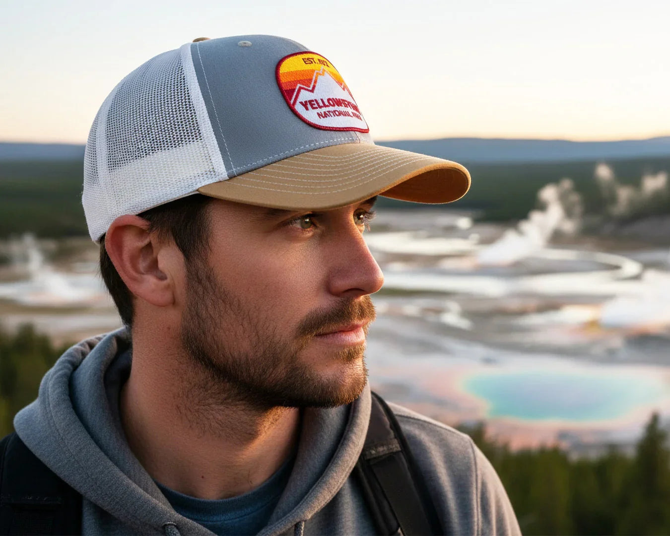Man wearing a cap with a Yellowstone National Park logo, standing in front of a scenic landscape.
