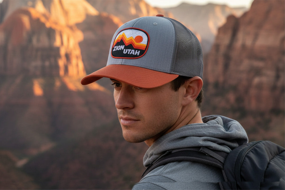 Man wearing a cap with Zion, Utah logo against a desert landscape