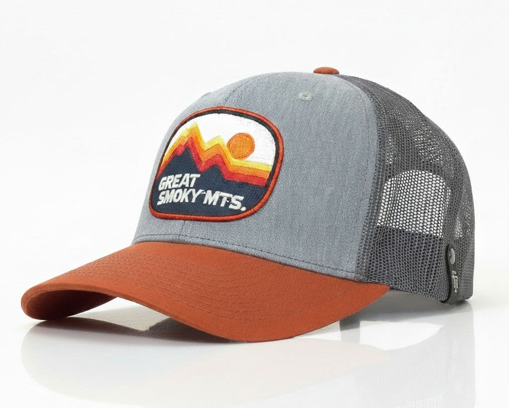 A Great Smoky Mountains trucker hat with a heather gray front panel and mesh back, a rust-orange curved brim, and a mountain-themed embroidered patch on the front.